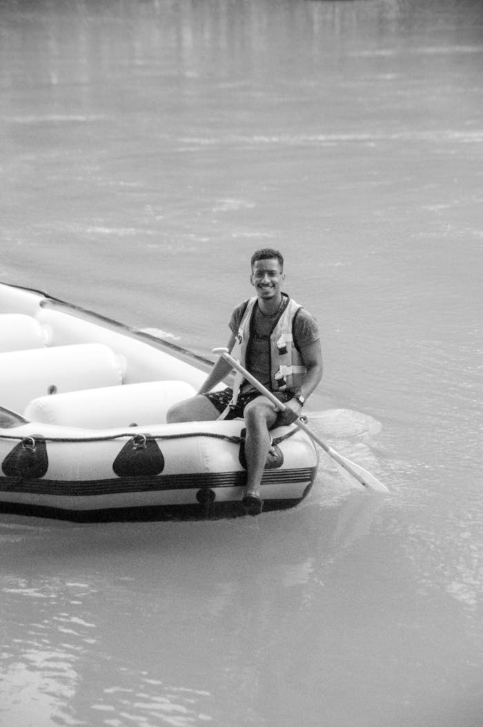 A man enjoying a rafting adventure on calm river waters in an inflatable boat.
